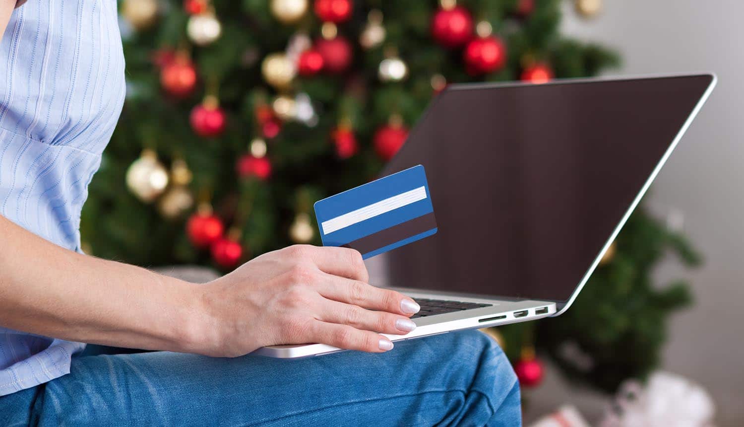 Image of woman holding credit card in front of laptop representing how online retailers are preparing for the holiday hacking season
