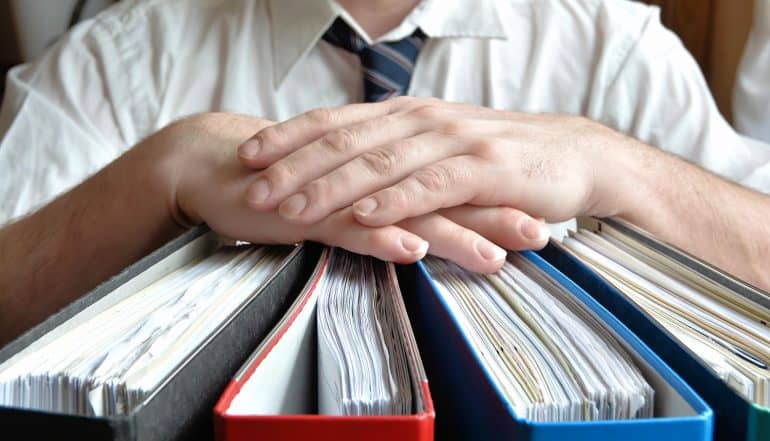 Image of businessman with hands resting on thick files representing protecting data subject rights for acccess, erasure and portability