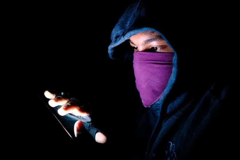 Image of hooded and masked man using a mobile phone signifying cyber espionage by hackers using fake apps with Android malware