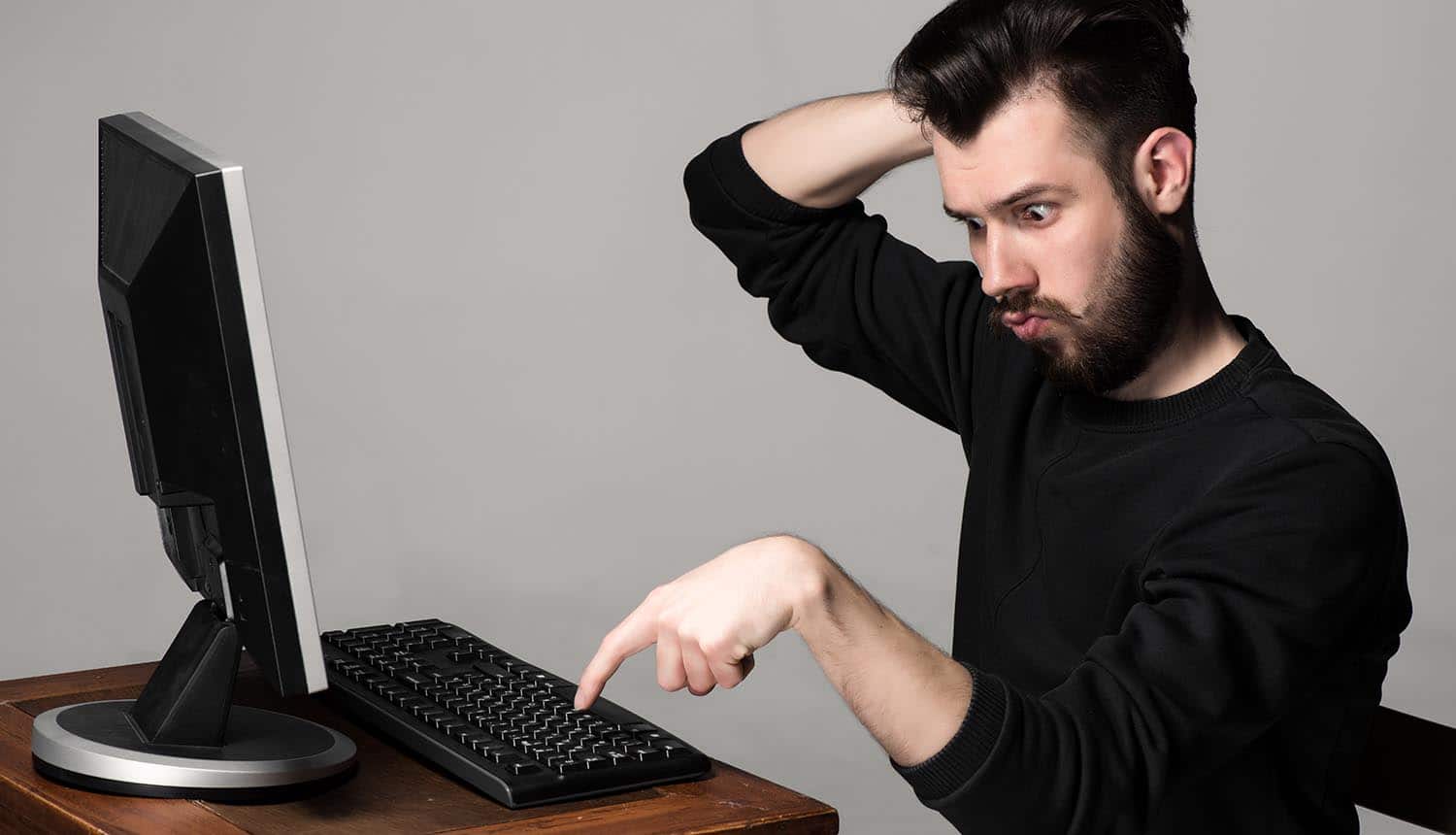 Image of confused man sitting in front of computer about to type signifying insider threats within the organization