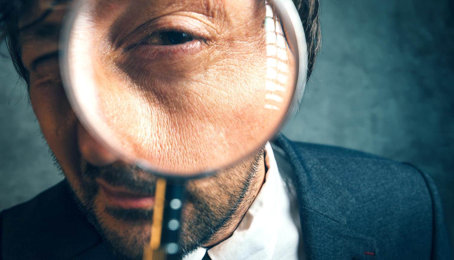 Image of man holding magnifying glass signifying executive taking care of business using a security to-do list