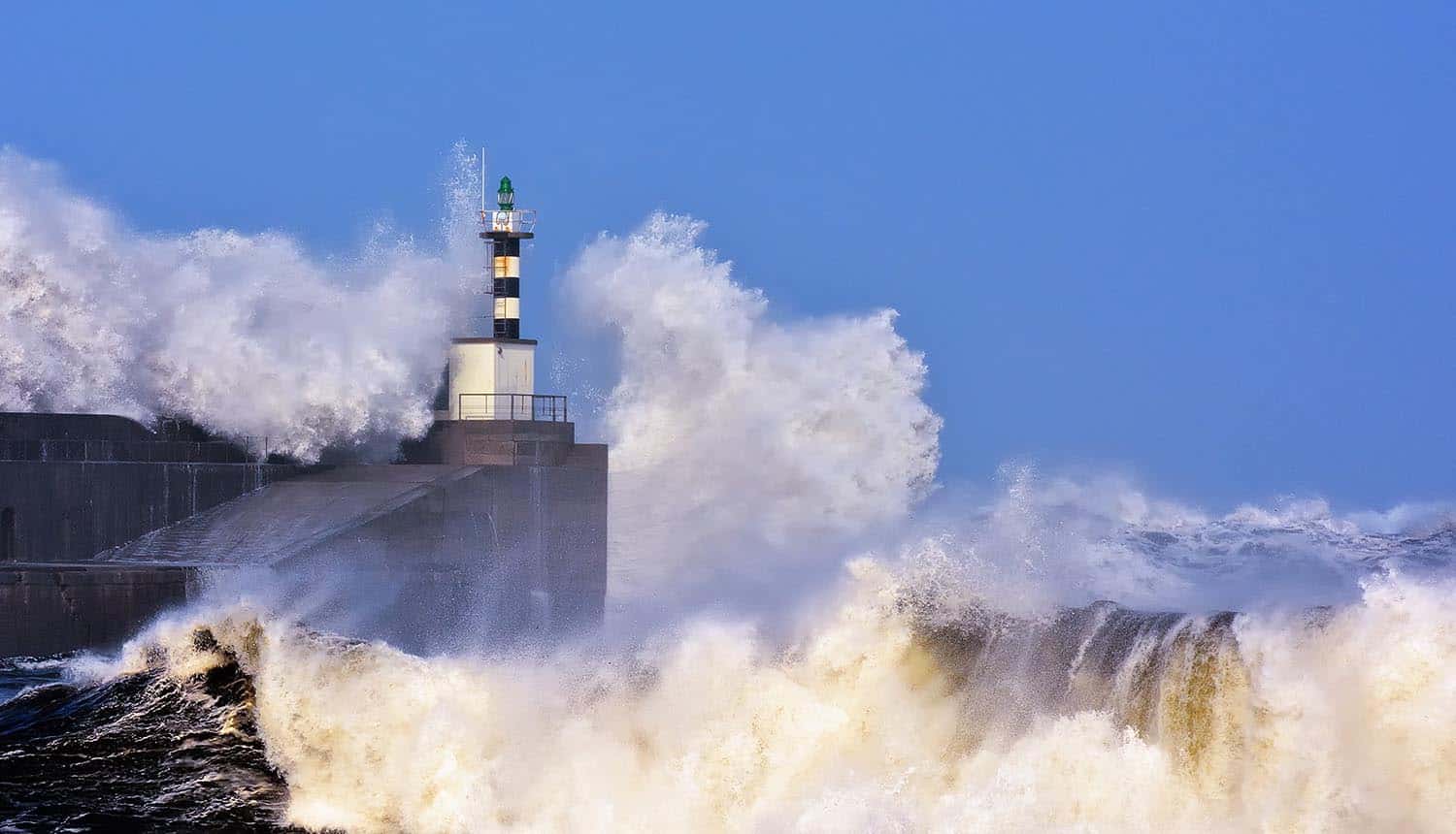Image of waves crashing on rocks around lighthouse signifying the waves of DDoS attack and the different attack vectors