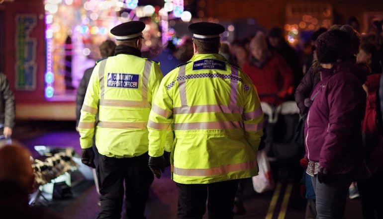 Image of two policemen walking along the street with onlookers signifying predictive policing and how that may result in biased arrests