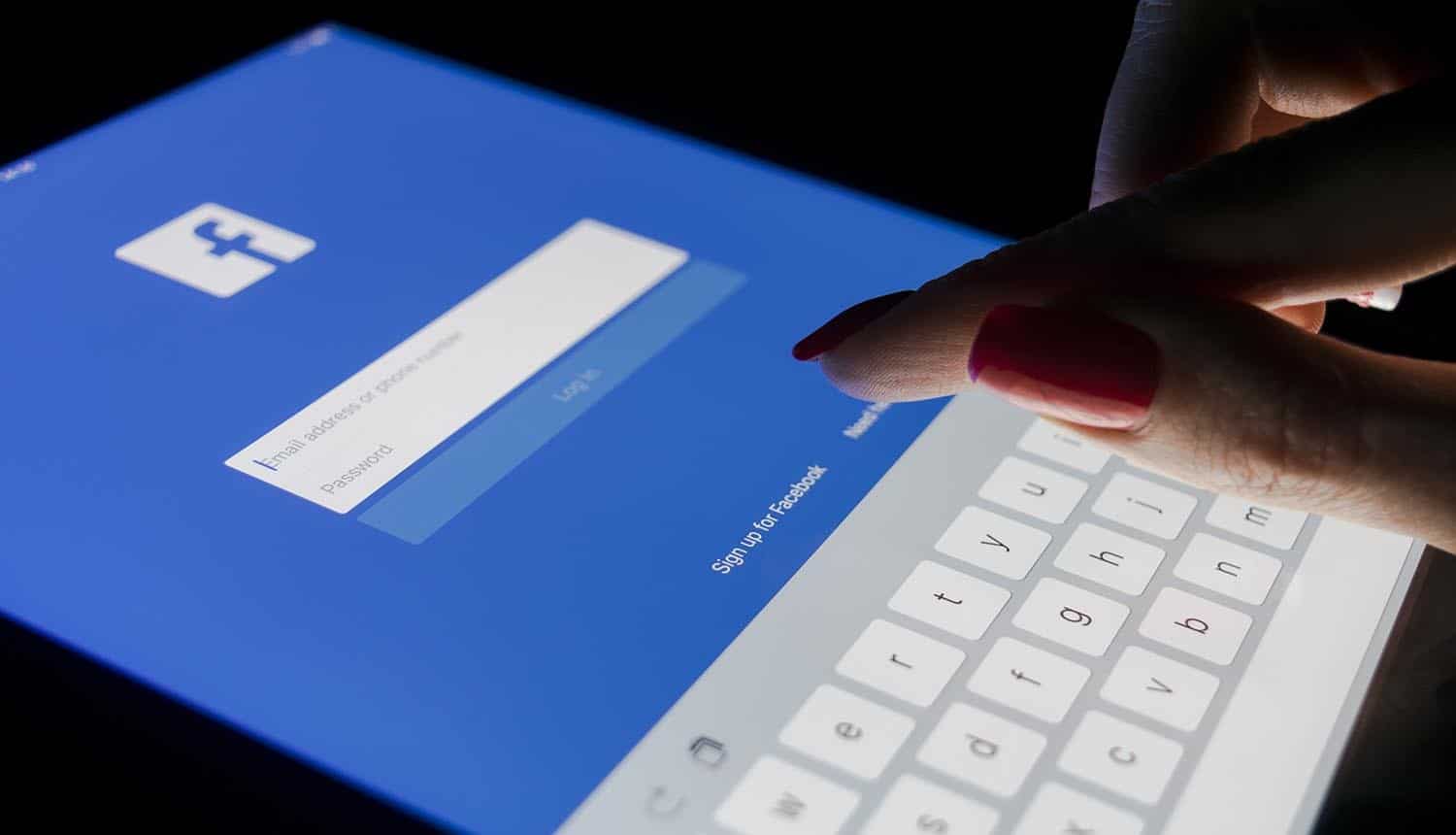 Image of finger tapping on ipad to login to facebook showing the idea of taking a closer look at the data scandal surrounding Facebook and Cambridge Analytica