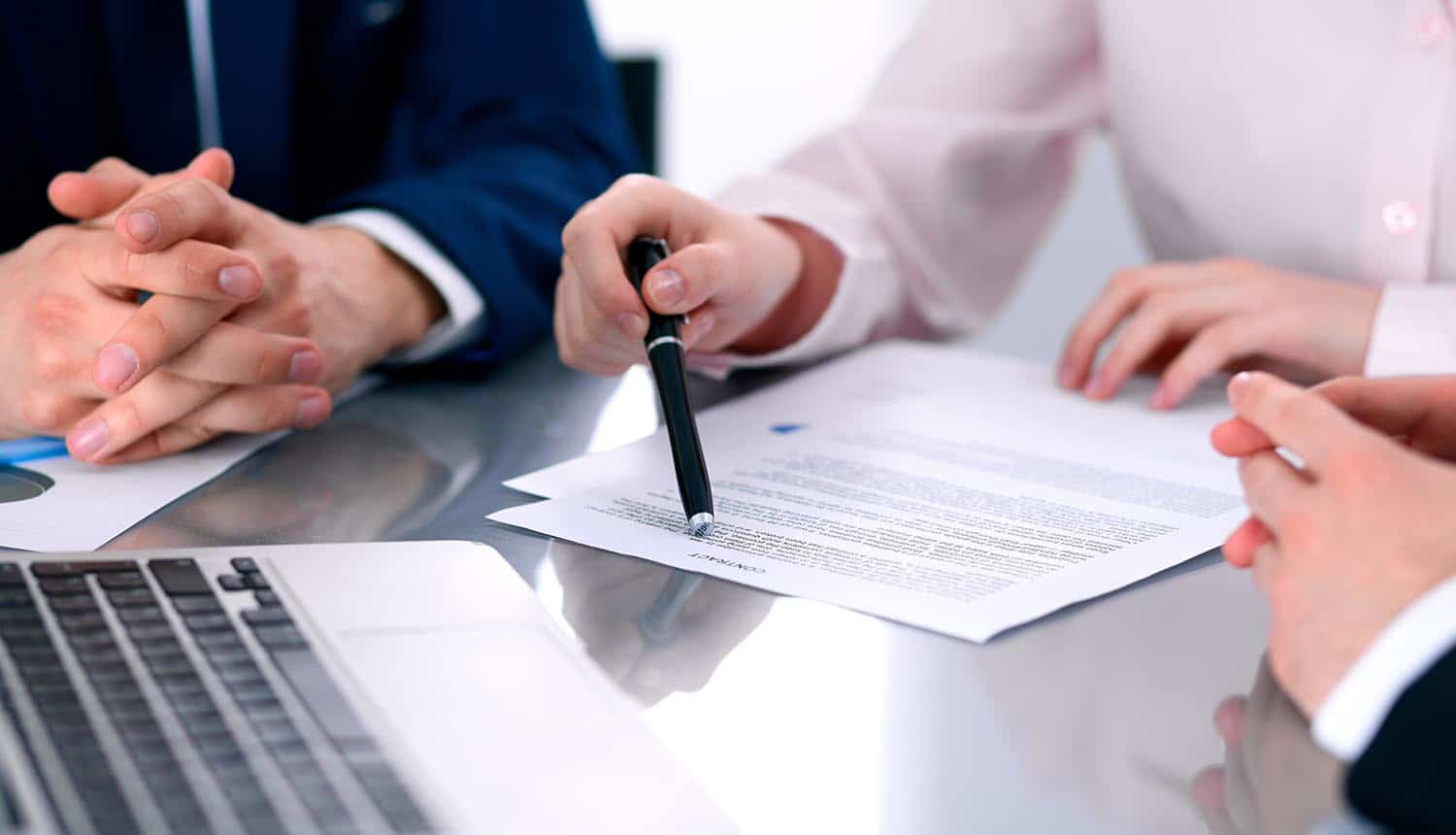 Image of woman explaining contract document in front of laptop to two men showing how there are lurking pitfalls in the blockchain contract era