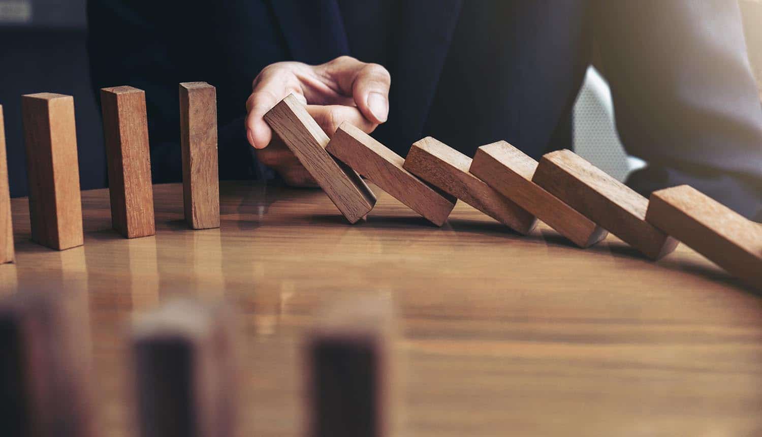 Image of man using finger to stop blocks falling like dominos signifying how contracted service providers can take down your business