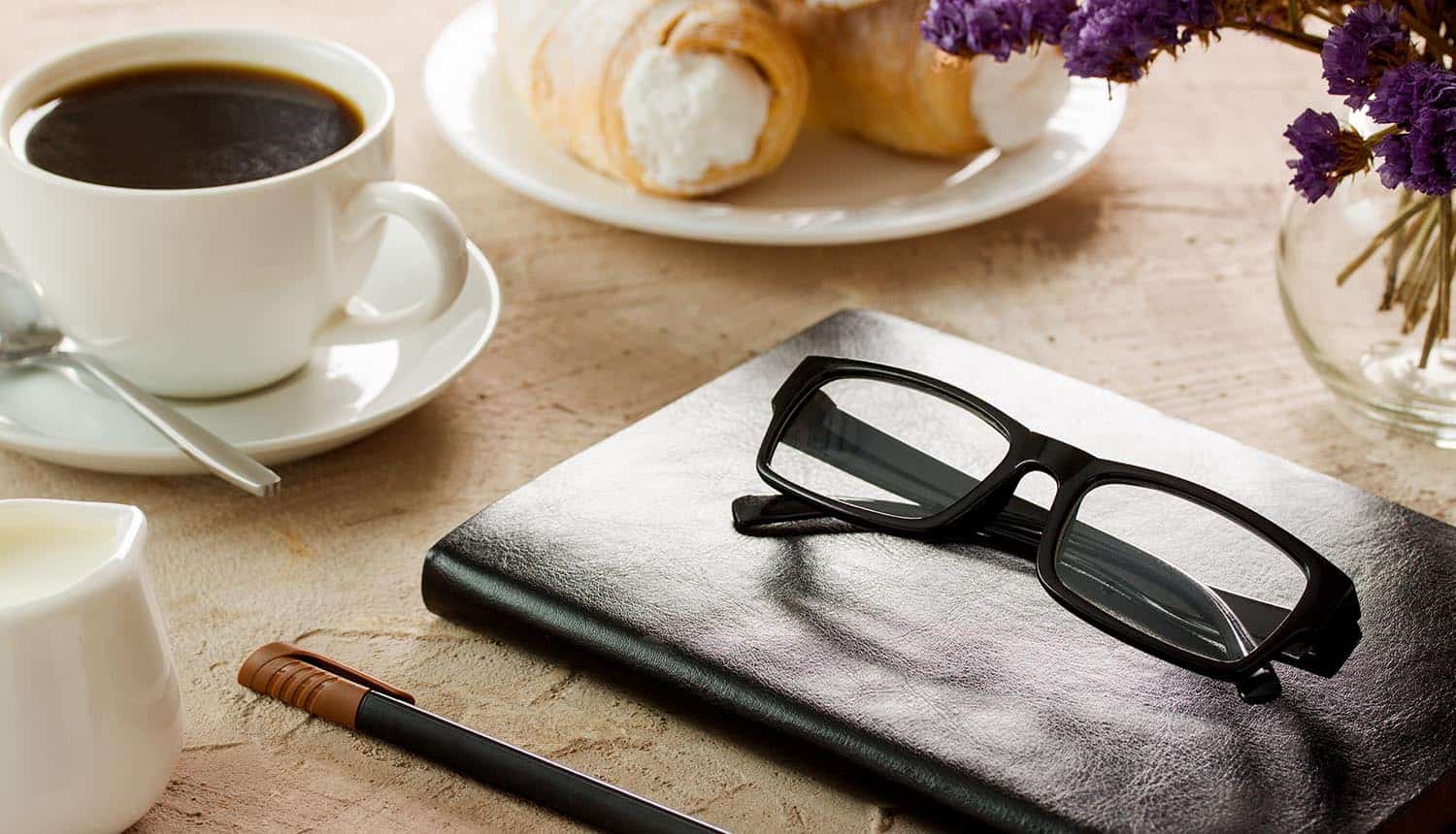 Black leather notepad, black-rimmed spectacles, white coffee cup and rolls with cream for a coffee interview with privacy leaders