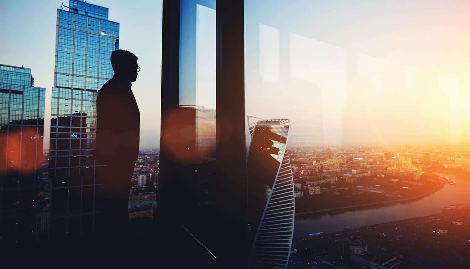 Silhouette of CEO looking out of big office window contemplating