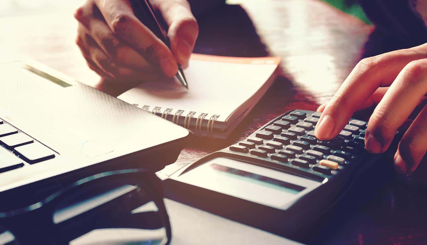 Close up woman hand using calculator and writing notes about cybersecurity spending