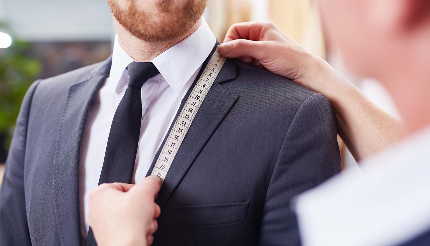 Tailor taking measurements of jacket to fit businessman showing personalization