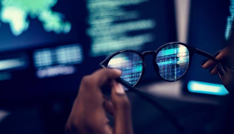 Hands holding glasses in front of computer screen to adopt a hacker's point of view