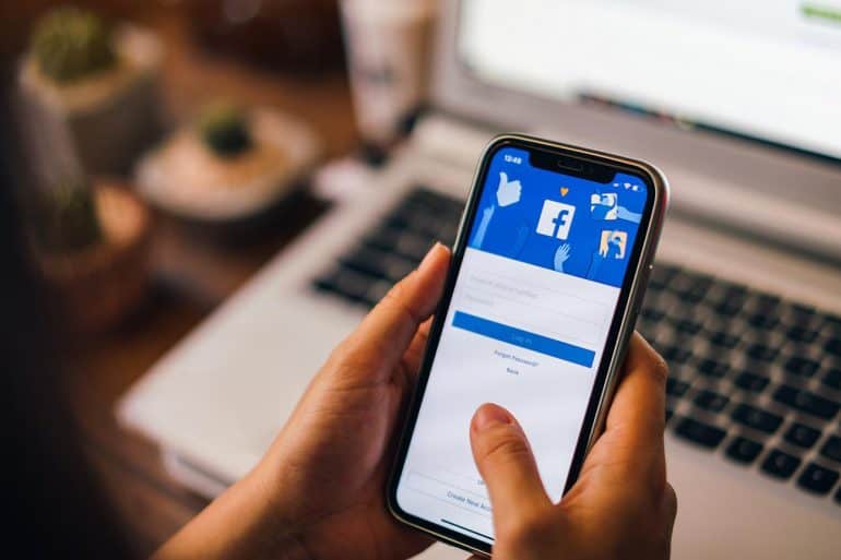 Woman holding a iPhone X and logging into Facebook after Facebook data breach which led to 50 million compromised accounts