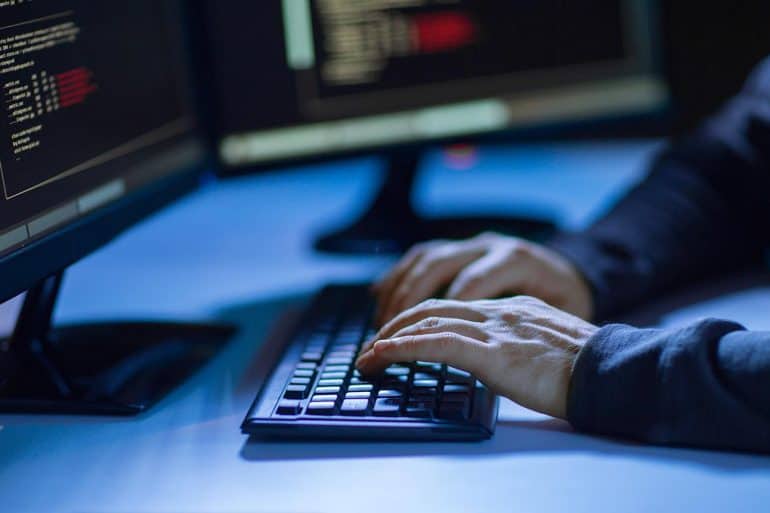 Hands of hacker in dark room writing code for cyber attack showing problem of cybersecurity skills shortage