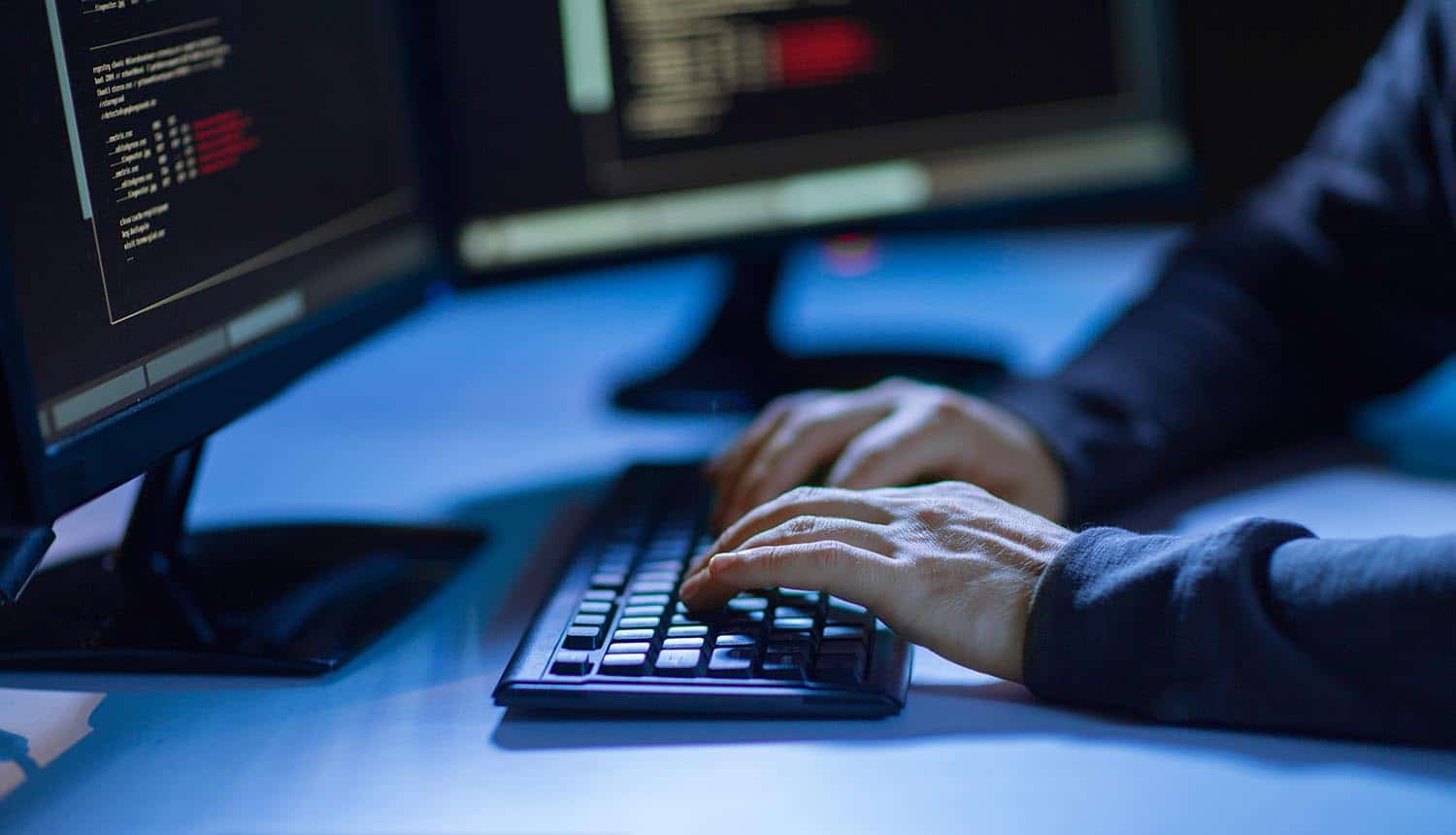 Hands of hacker in dark room writing code for cyber attack showing problem of cybersecurity skills shortage