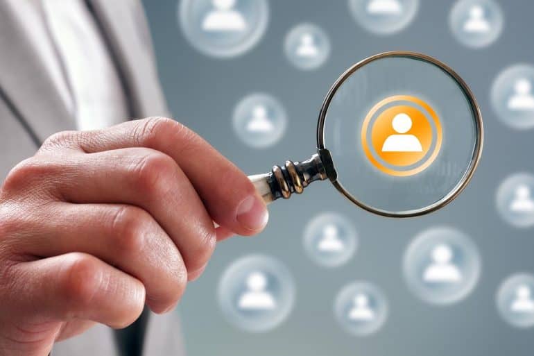 Businessman with magnifying glass on people icons showing targeted Facebook advertising and LinkedIn's privacy violation