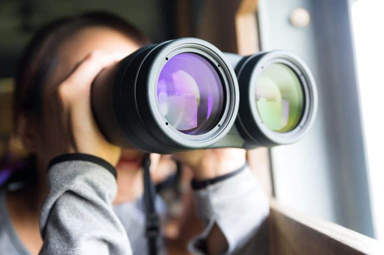 Young woman using binoculars to look into the future showing the need to look beyond regulations for the privacy industry