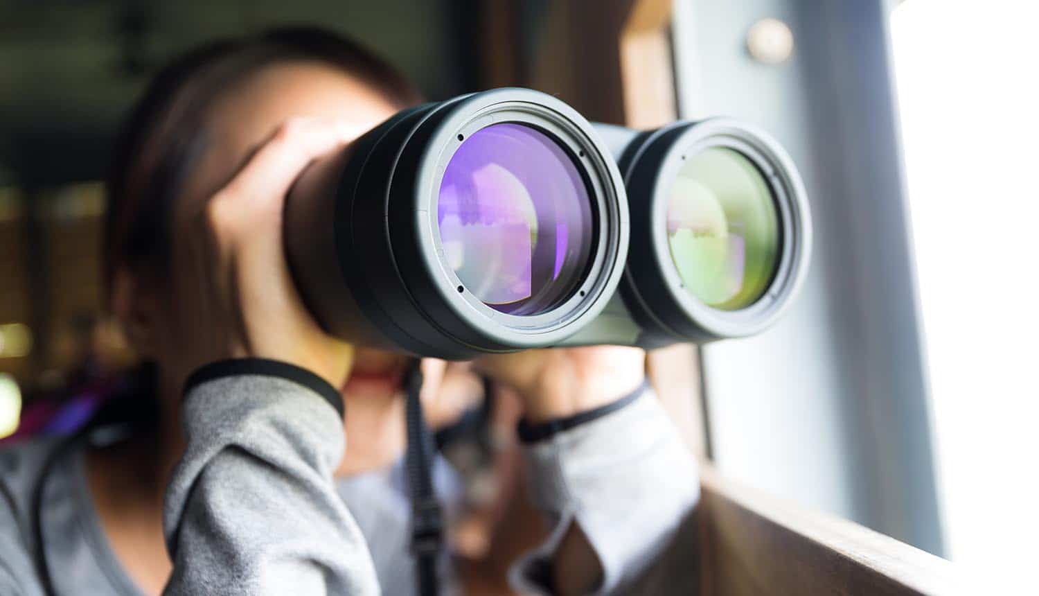 Young woman using binoculars to look into the future showing the need to look beyond regulations for the privacy industry