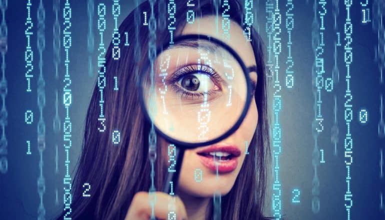 Curious woman looking through a magnifying glass against computer binary code background showing the extent of surveillance capitalism