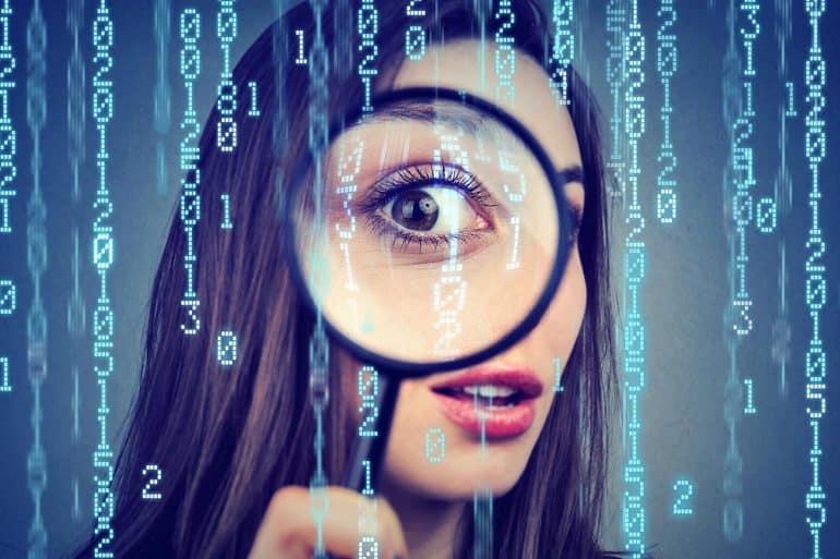 Curious woman looking through a magnifying glass against computer binary code background showing the extent of surveillance capitalism
