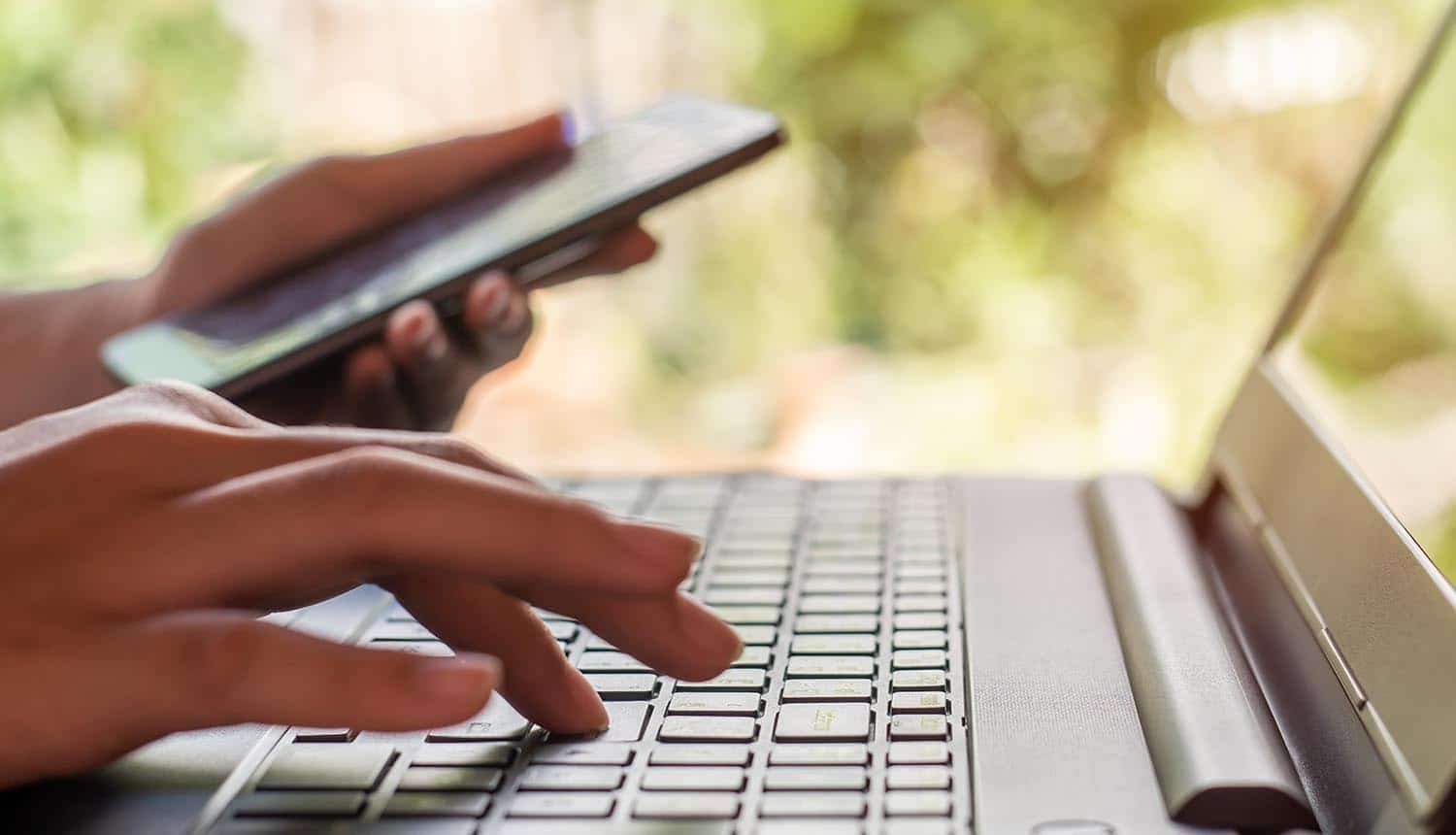 Hand with smart phone and laptop doing online shopping showing the account takeover fraud problem