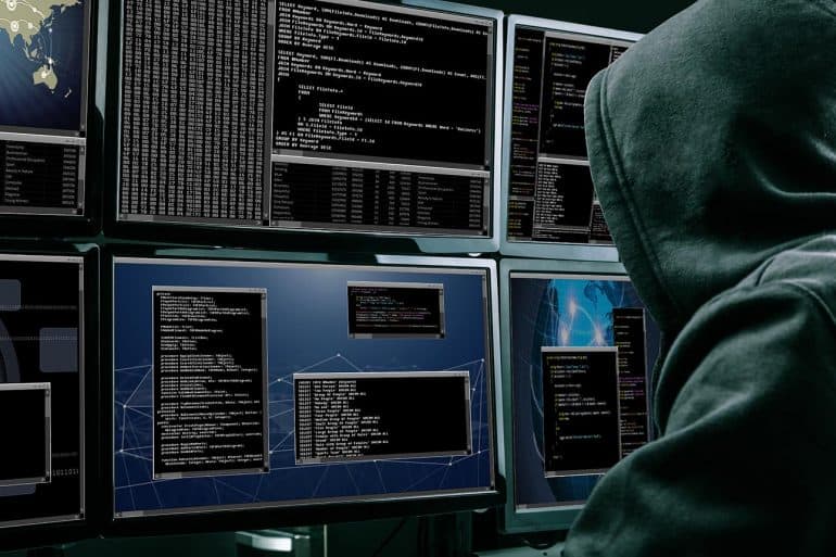 Rear view of a hacker using multiple computers for identity theft and cybercrime