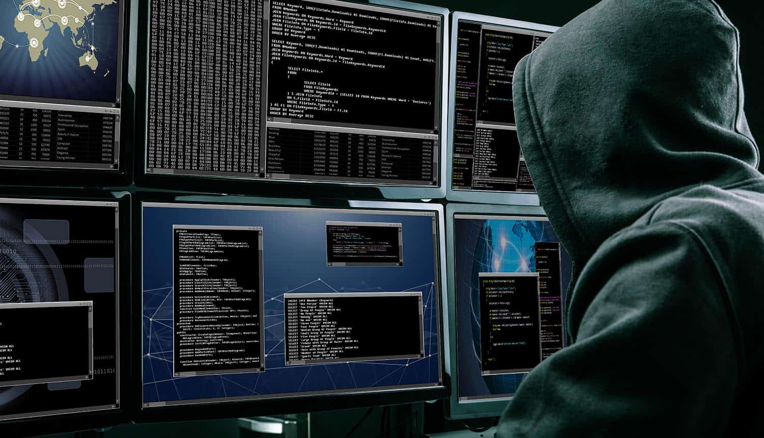 Rear view of a hacker using multiple computers for identity theft and cybercrime