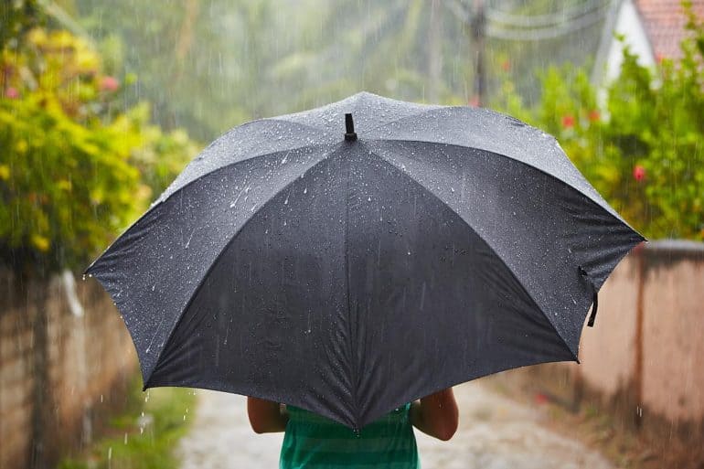 Woman with black umbrella in heavy rain showing the need for personal cyber insurance
