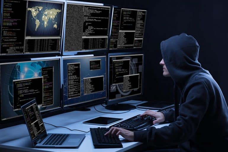 Rear View Of A Hacker Using Multiple Computers Showing Top Information Security Risks