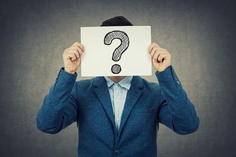 Man covering his face using a white paper with drawn question mark like a mask for hiding his identity.