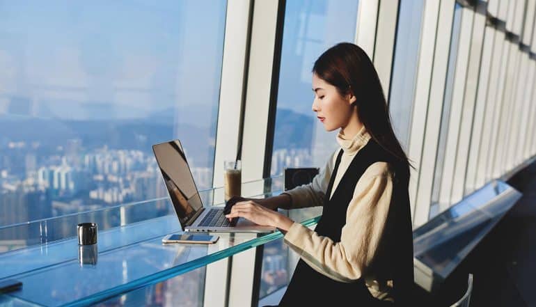 Woman working on her laptop near hotel window showing managing risk in the digital era