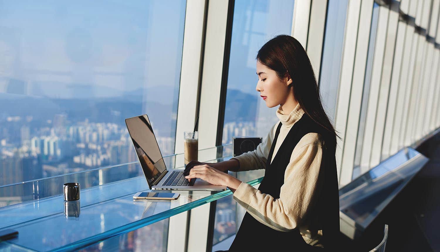 Woman working on her laptop near hotel window showing managing risk in the digital era
