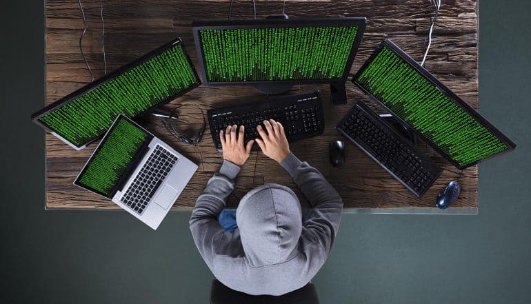 Hacker working on multiple computers showing the impact of data breach by Iranian hackers