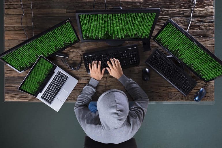 Hacker working on multiple computers showing the impact of data breach by Iranian hackers