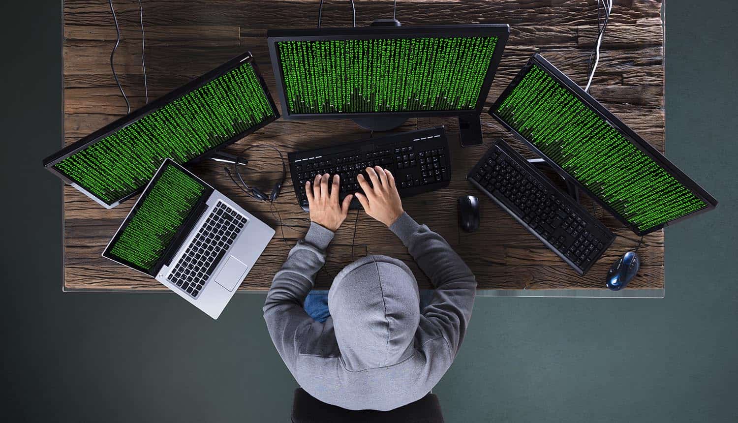 Hacker working on multiple computers showing the impact of data breach by Iranian hackers