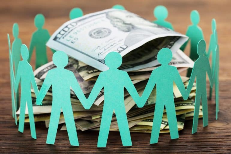 Paper cut out human figures around stack of hundred dollar bills showing concept of digital dividends and data monetization revenue sharing