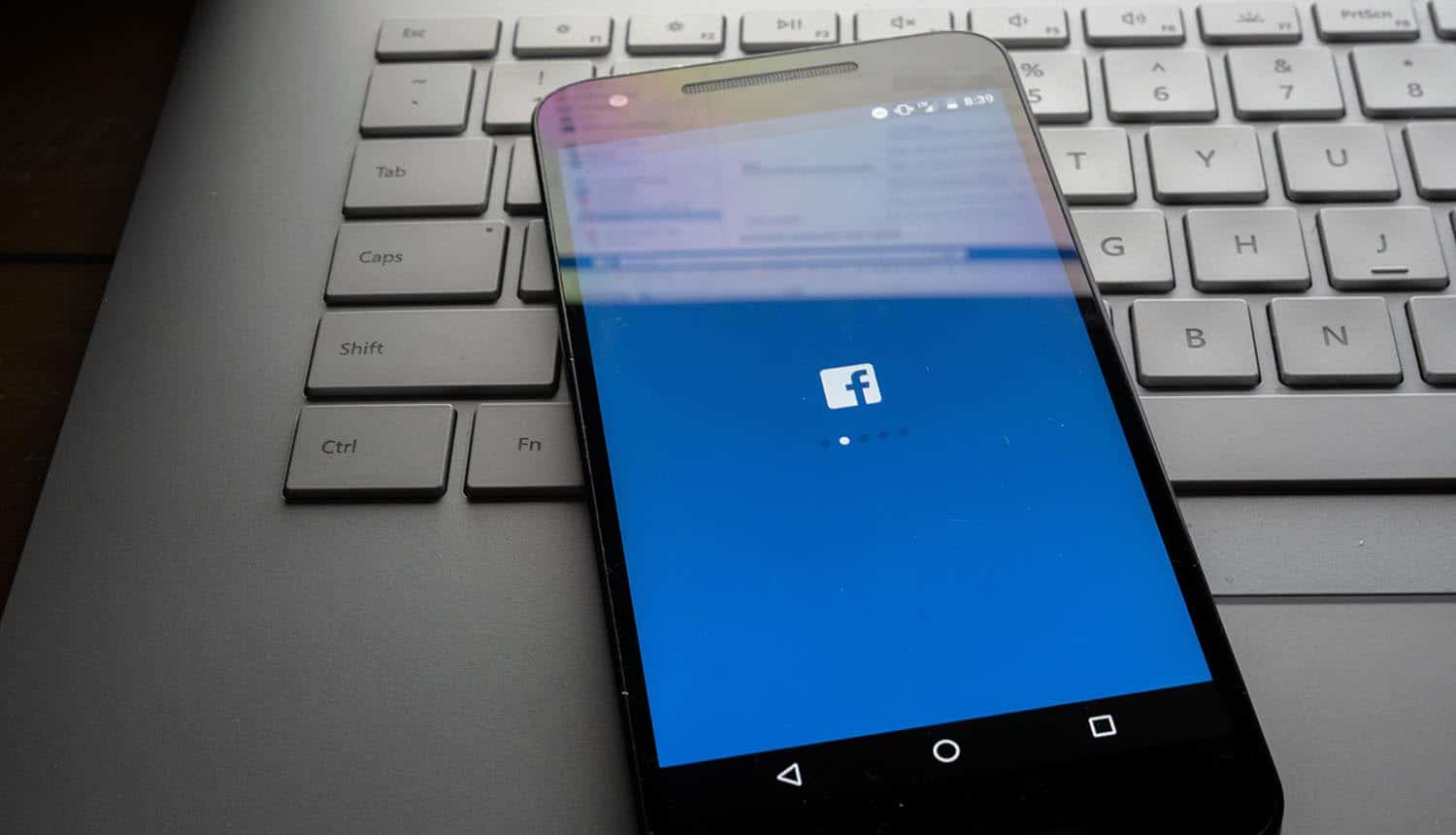 Facebook app on phone sitting on laptop showing Facebook cybercrime groups using the social media platform to conduct cybercrime activities