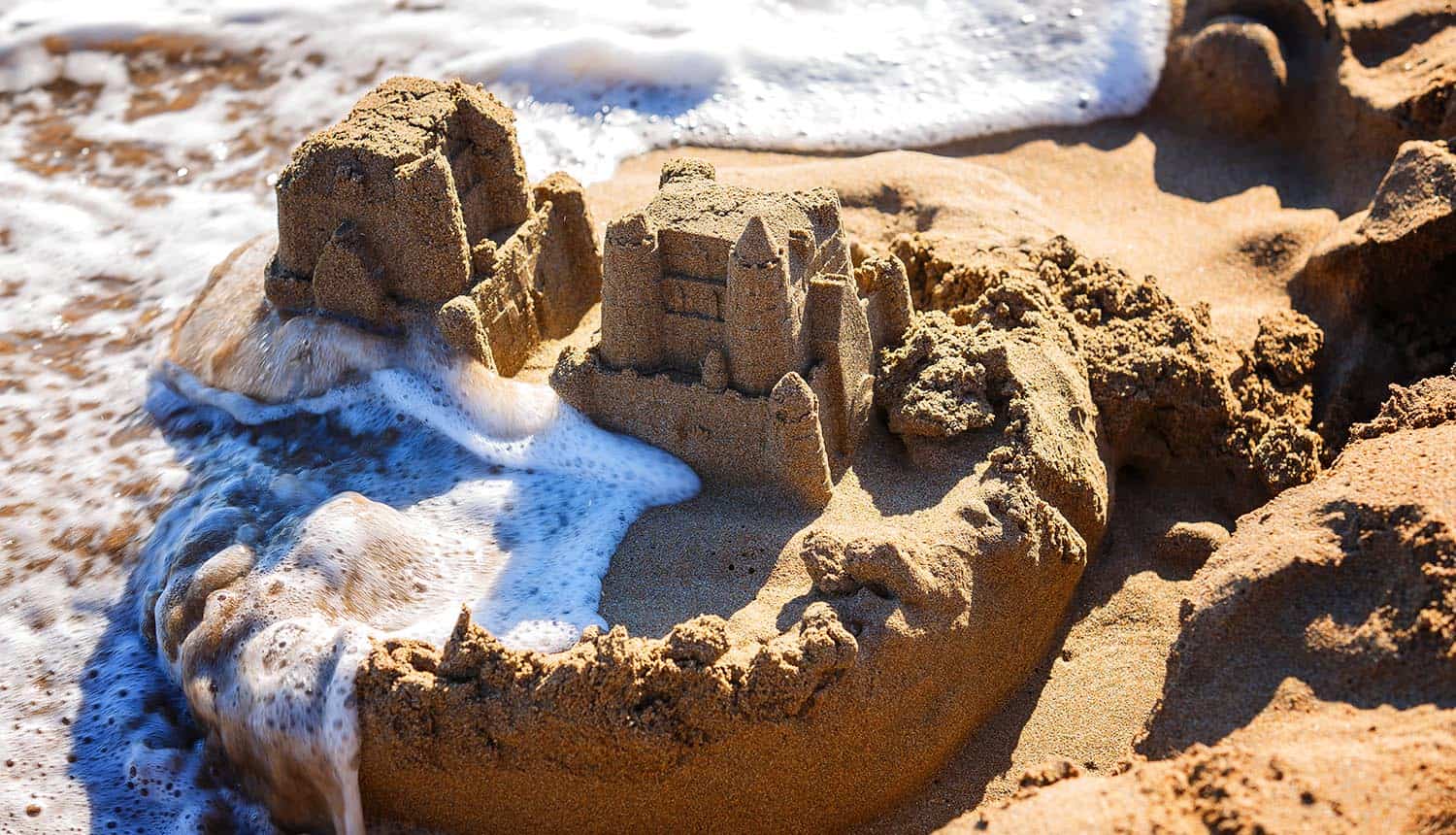 Waves wash away sand castles on the beach showing how businesses have trouble achieving cyber resilience