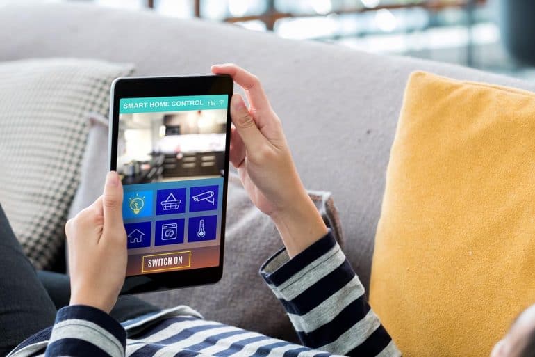 Hand on tablet using smart home system showing new IoT security laws in U.K. and U.S. to protect consumers from hacks of internet-connected devices