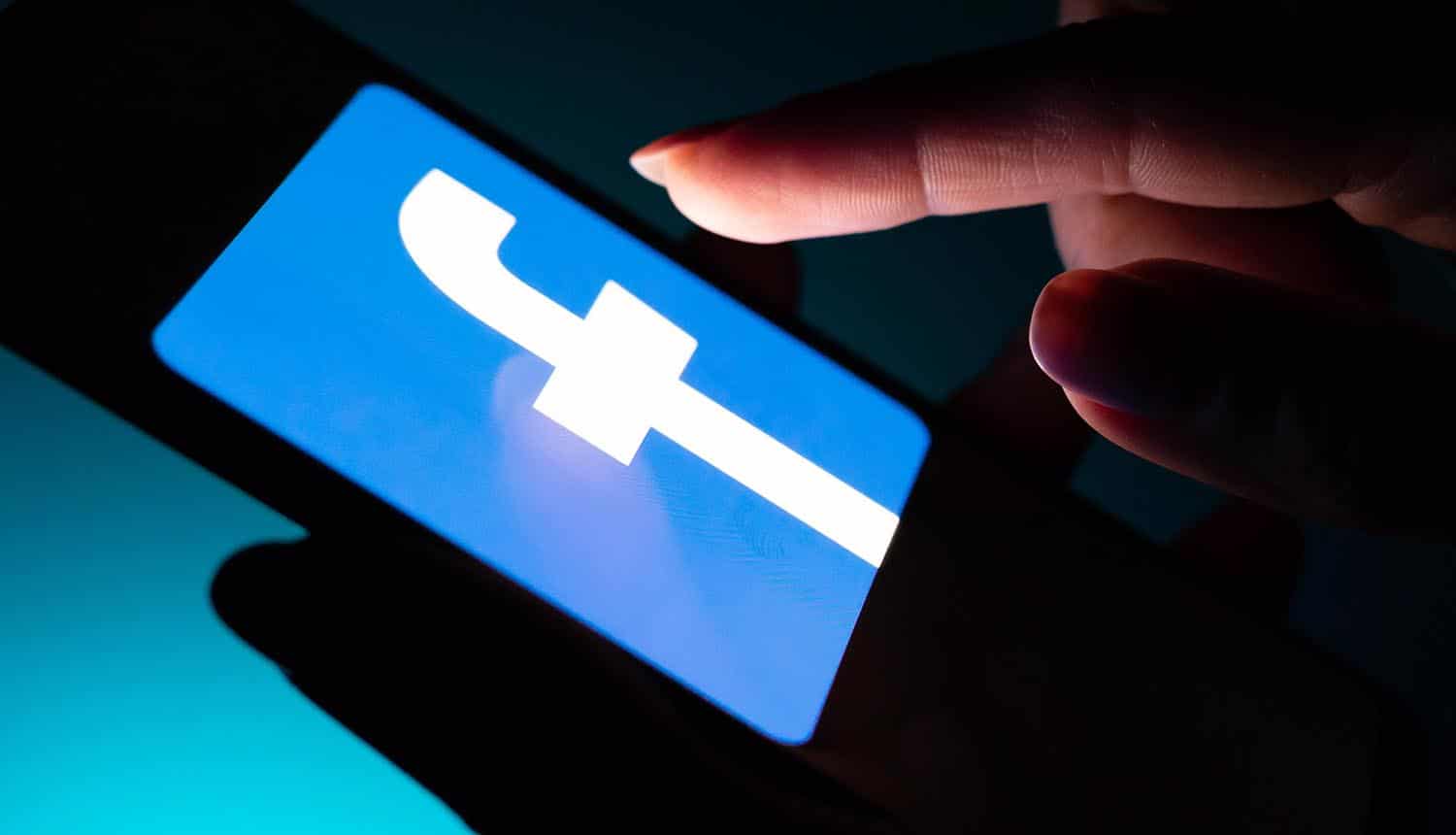 Man touching Facebook app on mobile showing potential privacy implications with Facebook’s Libra cryptocurrency