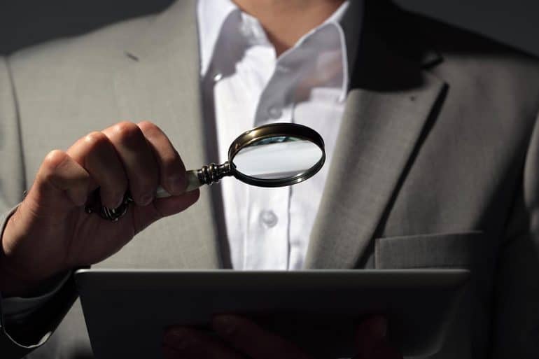 Businessman looking at tablet through magnifying glass showing the role of investor in boosting global cyber security as outlined in new WEF report