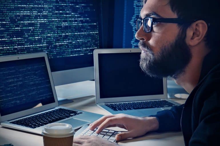Young man hacking server in dark room showing the concerns of proposed Active Cyber Defense Bill for companies to “hack back”