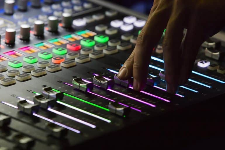 Hand on audio mixing board showing the rising use of deepfake audio to run AI cyber attacks
