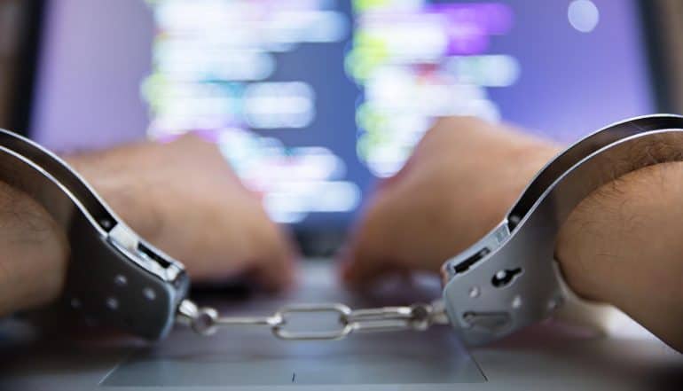Hands in handcuffs using laptop showing how technology has transformed insider fraud and yet being used in fighting back