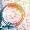 Magnifying glass lies on paper showing recent IBM-Ponemon study highlighting the rising cost of a data breach
