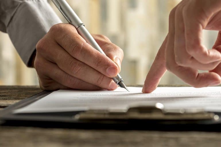 Businessman pointing to his business partner where to sign an agreement showing the terms, conditions and considerations under GDPR