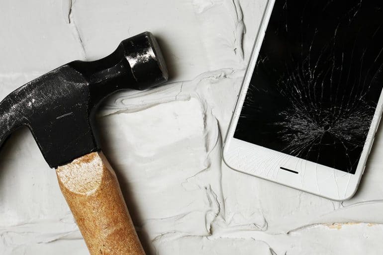 Broken iPhone with hammer on brick background showing the massive challenge of mobile device security with major watering hole attack on iOS