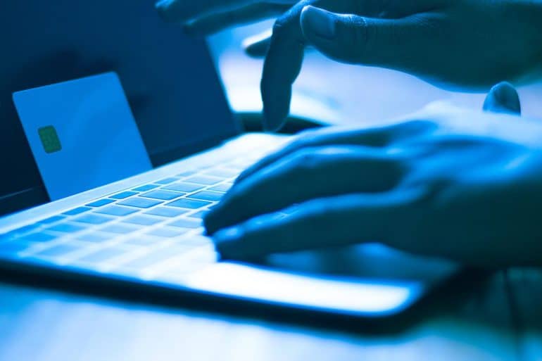 Hacker with credit card on laptop showing the biggest credit card database for sale on Joker’s Stash
