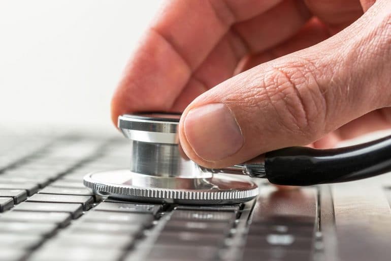 Man checking the health of his laptop computer using a stethoscope showing malware threats targeting Macs outpaced Windows