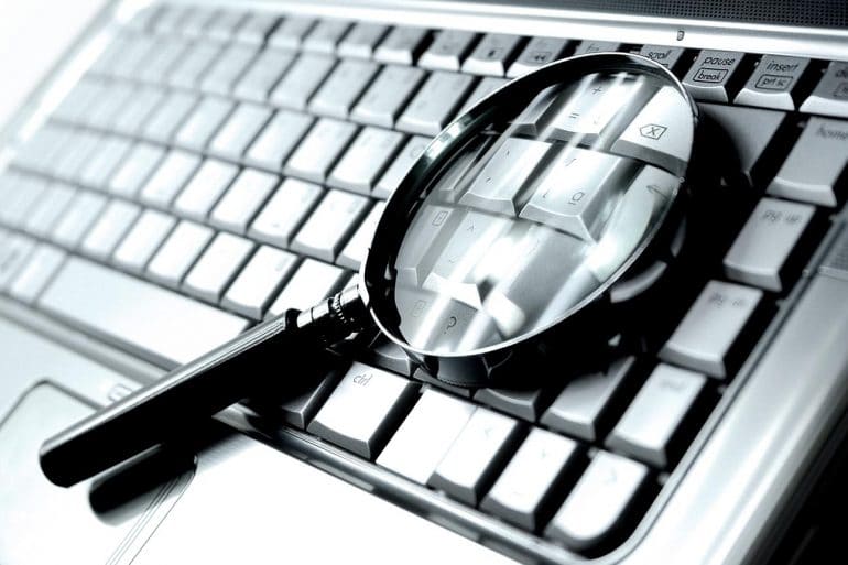 Magnifying glass on laptop keyboard showing the adversary attribution approach to fight cybercrime