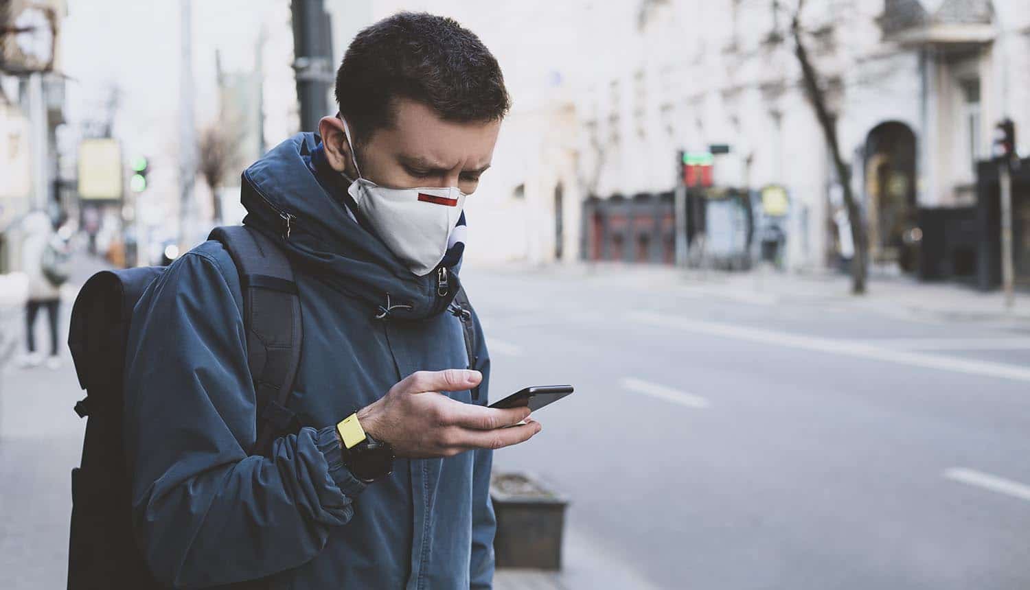 Man in mask using mobile on the street showing the attempt to balance public health measures with user privacy for contact tracing apps